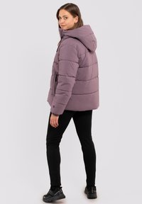Puffjakke i dæmpet lavendel, med hætte, elastiske manchetter og en taljebælte. Kombinationen er med sorte leggings og solide sorte fodtøj.