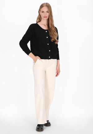 Zwarte geribbelde cardigan met een ronde hals en zes knopen. Gecombineerd met crèmekleurige wijde broek en zwarte schoenen. Gladde textuur.