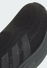 Čierne pletené tenisky s textúrovaným zvrškom, so tromi horizontálnymi gumovými pruhmi a zaoblenou podrážkou.