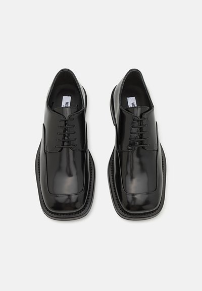 Black patent leather shoes with a square toe, six lace eyelets, and contrasting textured sole. Smooth surface with minimal embellishments.