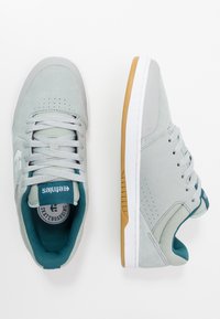 Šedé semišové skateboardové boty s tyrkysovými detaily, perforovaným designem a bílou podrážkou. Kulatá špička a polstrované vnitřní vyložení pro pohodlí.