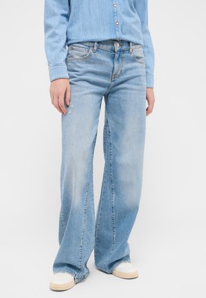 Helle blaue, ausgeweitete Denim-Jeans mit verblassten Bereichen, subtiler Abnutzung und traditionellem Five-Pocket-Design. Getragen mit weißen Sneakers.