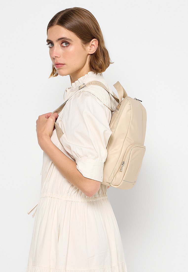 Beiger Nylon-Rucksack, der über eine Schulter getragen wird, mit einer Reißverschlusstasche auf der Vorderseite und verstellbaren Trägern, einer glatten Textur und minimalistischen Design.