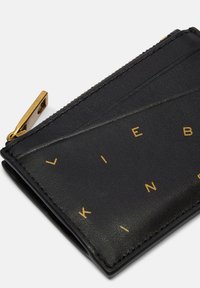 Czarny skórzany portfel z metalicznym złotym logo i zamkiem błyskawicznym. Teksturowana powierzchnia z ukośnymi detalami wzoru.
