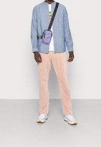 Blå skjorta med knappar, vit t-shirt med grafik, rosa kordbyxor, lila axelväska med svart rem, vita sneakers med bruna detaljer.