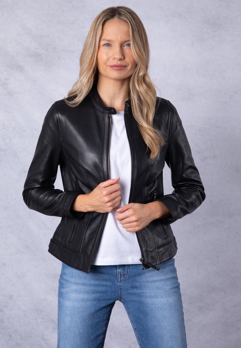 Black leather jacket with a stand collar, front zipper, and side pockets. The material is smooth with a fitted design. Worn over a white top.