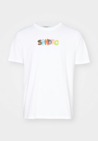 T-shirt en coton blanc à manches courtes arborant un logo flou et coloré "SANDRO" au centre dans des nuances de bleu, orange et vert.