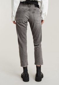 Jean en denim gris avec une jambe fuselée, poches visibles et un ourlet légèrement effiloché. Associé à des bottines noires.