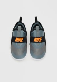 Sneakers Nike slip-on grigie e nere con logo arancione sulle cinghie, suole bianche e linguette, viste dall'alto su sfondo bianco.