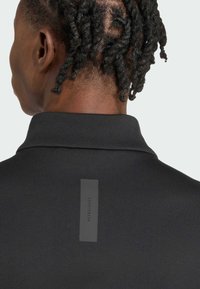 Ropa deportiva negra con una tela texturizada, que presenta un cuello y una etiqueta rectangular en la parte posterior con "SPORTSWEAR" impresa en gris.