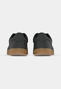 Paire de baskets basses noires avec semelles en caoutchouc marron vues de dos sur un fond clair uni.