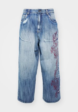 Világoskék farmernadrág, széles szárú szabással, melyen kopottas részletek és bonyolult piros hímzett díszítések találhatóak az oldalon.