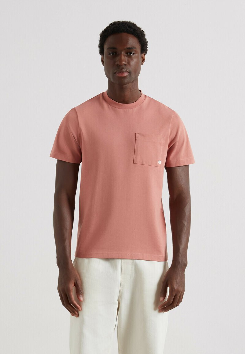 Korte mouwen T-shirt in zacht koraal, met een ronde halslijn en een borstzakje. Gemaakt van lichte stof met een gladde textuur.