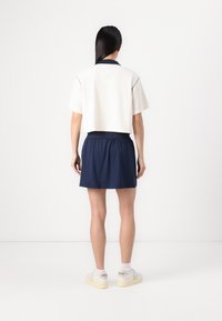 Polo shirt blanc court avec col marine associé à une jupe-short marine. Les chaussures sont des baskets légères avec des accents contrastants.