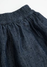 Dżinsowa spódnica z elastycznym paskiem w talii, w ciemnoniebieskim kolorze, z marszczonym wzorem i małymi kropeczkami na całej powierzchni.