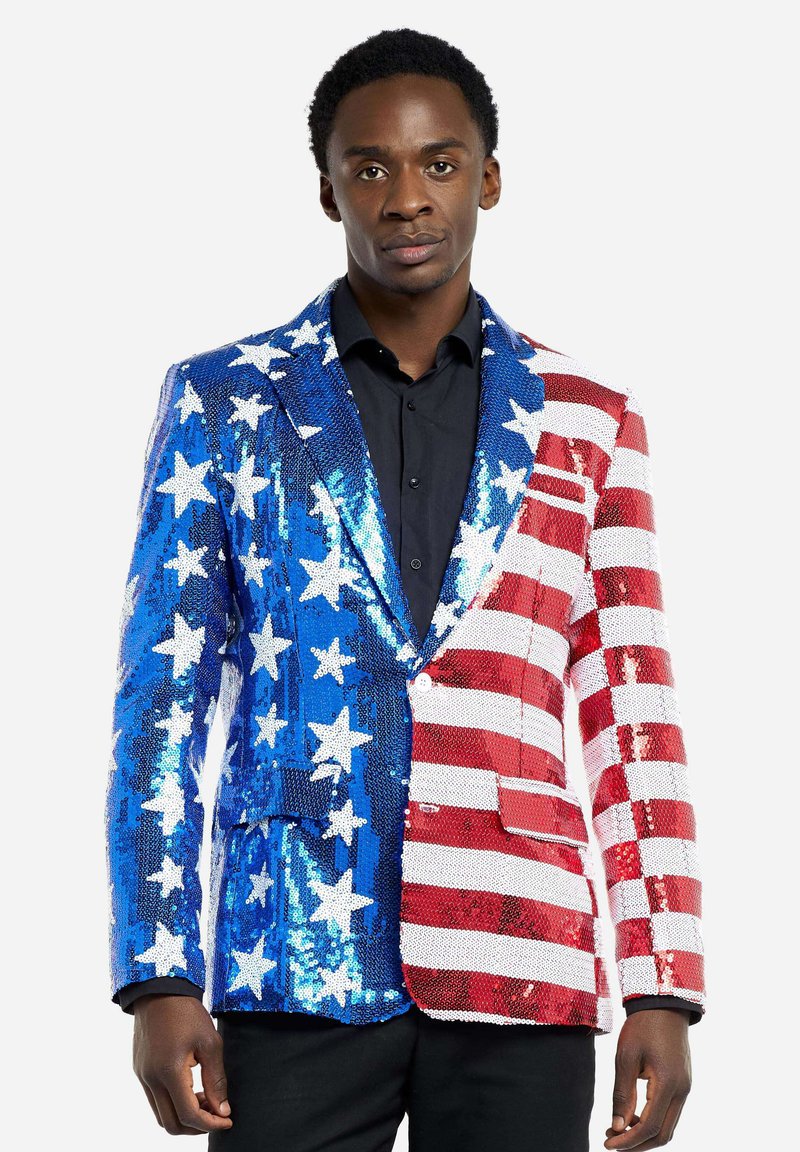 Svetrový blazer s flitrami, ktorý na jednej strane má modré pozadie s bielymi hviezdami a na druhej strane červené a biele pruhy. Štruktúrovaný dizajn, s výrezom na klopách a jedným gombíkom na zapínanie.