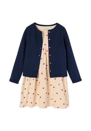 Navy blue long-sleeve cardigan over a beige dress with a pattern of small red hearts, buttoned down the front.