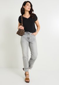 Top negro de manga corta con borde de encaje, jeans de tiro alto en gris claro y sandalias de tacón marrones. Un bolso de estampado de leopardo complementa el conjunto.