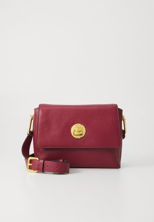 Burgundy leather crossbody bag with a flap, gold circle clasp, and adjustable strap. Textured surface with a smooth interior finish.