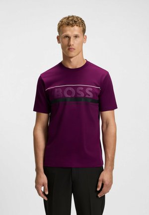 T-shirt viola a maniche corte realizzata in tessuto liscio, con una striscia orizzontale nera con la parola "BOSS" in un carattere audace attraversando il petto.