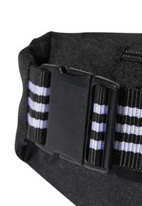 Sac en tissu noir avec une boucle en plastique noir et des rayures alternées noires et lavande sur la sangle ajustable.