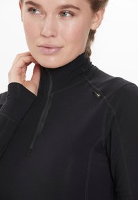 Sort lynlås mock neck top med en tætsiddende pasform, glat stof, synlige stikninger og et lille logo tag på kraven.