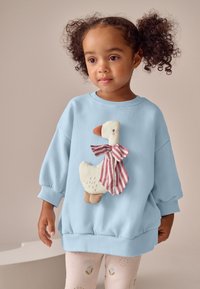 Blauer Pullover mit einer flauschigen Enten-Applikation, die eine gestreifte Fliege trägt. Verfügt über lockere Passform und gerippte Bündchen. Kombiniert mit gemusterten Leggings.