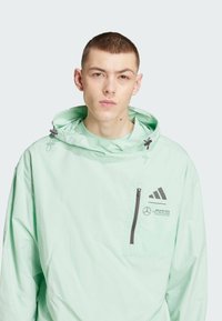 Jasno miętowa kurtka z kapturem, z zamkiem błyskawicznym, czarnymi akcentami oraz logo Adidas i Mercedes-AMG Petronas.