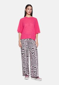 Rosa, übergroßer Strickpullover mit Rundhalsausschnitt, kombiniert mit schwarz-weißen karierten Weitbein-Hosen mit abstrakten Mustern.