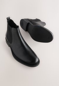 Čierne kožené Chelsea topánky s elastickými bočnými panelmi, zaoblenou špičkou a hladkým povrchom. Majú textúrovanú gumovú podrážku pre lepšiu priľnavosť.