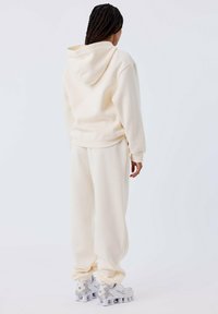 Sudadera color crema y joggers a juego, confeccionados con una tela suave, que presentan un corte relajado, puños acanalados y un bolsillo canguro.