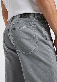 Jeans in denim grigio con un taglio aderente, caratterizzati da un'etichetta in pelle nera in vita, tasche posteriori con cuciture sottili e dettagli in metallo dorato.