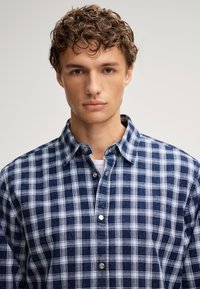 Camicia a scacchi blu e bianca con colletto alla francese, realizzata in un tessuto testurizzato e con bottoni argentati sulla pattina.