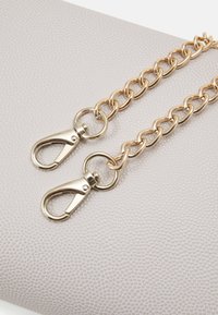 Guldmetallkedja med två krokfästen, fäst vid en strukturerad ljusgrå yta, som visar blanka ytor och sammanlänkade länkar.