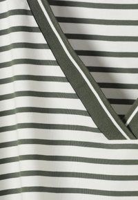 Λευκό ύφασμα με οριζόντιες ελιές πράσινες ρίγες και ντεκολτέ σε σχήμα V με ραβδωτή πράσινη ταινία με λεπτή λευκή ρίγα.