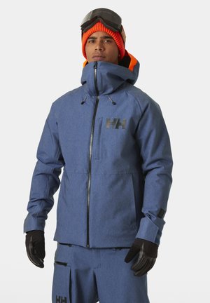 Giacca da sci blu con colletto alto, zip frontale e logo nero. Presenta cordini regolabili e polsini aderenti. Da abbinare a guanti neri.