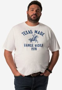 T-shirt blanc à manches courtes avec un imprimé graphique bleu représentant un cow-boy sur un cheval, avec le texte "TEXAS MADE RANGE RIDER 1978".