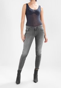 Šedé skinny džíny s distressed detaily a středním pasem, spárované s námořnickou tílkou a šedými kotníkovými botami. Hladká struktura látky.