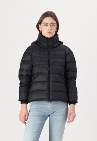 Svart pufferjakke med høy krage, glidelås lukking, og sidelommer. Har ribbestrikkede mansjetter og kontrasterende striper på skuldrene.