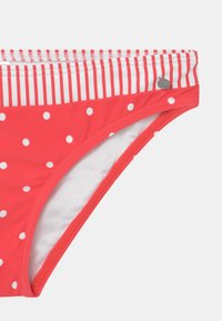 Rote Bikiniunterhose mit weißen Streifen am Bund. Hergestellt aus weichem Material und mit einem silbernen Logo-Akzent an der Seite.