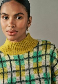 Strikket sweater med en gul ribbet turtleneck, der har et flerfarvet ternet mønster i grøn, teal, gul og hvid, med teksturerede fibre.