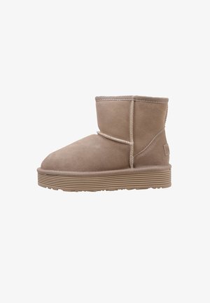 Bottine en suède beige avec semelle en caoutchouc épaisse, couture visible et bout arrondi et doux, présentée en profil latéral sur fond blanc.