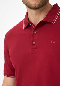 Brax rød polo skjorte med struktureret stof, to knapper og kontrastfarvet hvid kant på kraven og ærmeender.