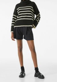 Pull à rayures noires et crème avec col roulé, associé à un short plissé noir et des chaussures noires épaisses, avec des accents côtelés.