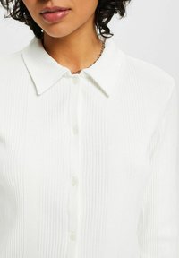 Vit ribbad knapp-up skjorta med spetsig krage, som har ett texturerat tyg och fem knappar fram.