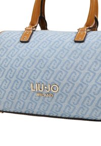 Blauwe canvas handtas met lichtblauw geometrisch patroon, bruine leren handvatten en metalen logodetail met de tekst "LIU JO MILANO."