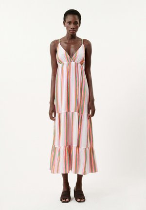 Robe maxi à bretelles blanche avec des rayures verticales arc-en-ciel. Elle possède un décolleté en V, un buste froncé et un ourlet en tiers avec volants.