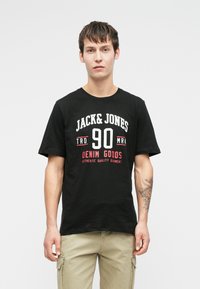 Tricou din bumbac negru cu mâneci scurte și guler rotund. Imprimarea de pe față prezintă "JACK & JONES" și "DENIM GOODS" în text alb și roșu.