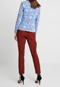 Floral print blazer in light blue with gold accents, paired with fitted burgundy pants, and black strappy heels for a sleek silhouette.