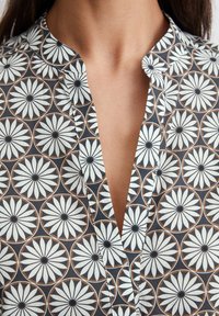 Poitrine et cou d'une femme portant une chemise sombre avec un motif floral de marguerite blanche et un décolleté en V sans boutons.
